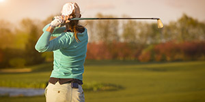 Close up of female golf player swinging golf club on fairway during sunset.